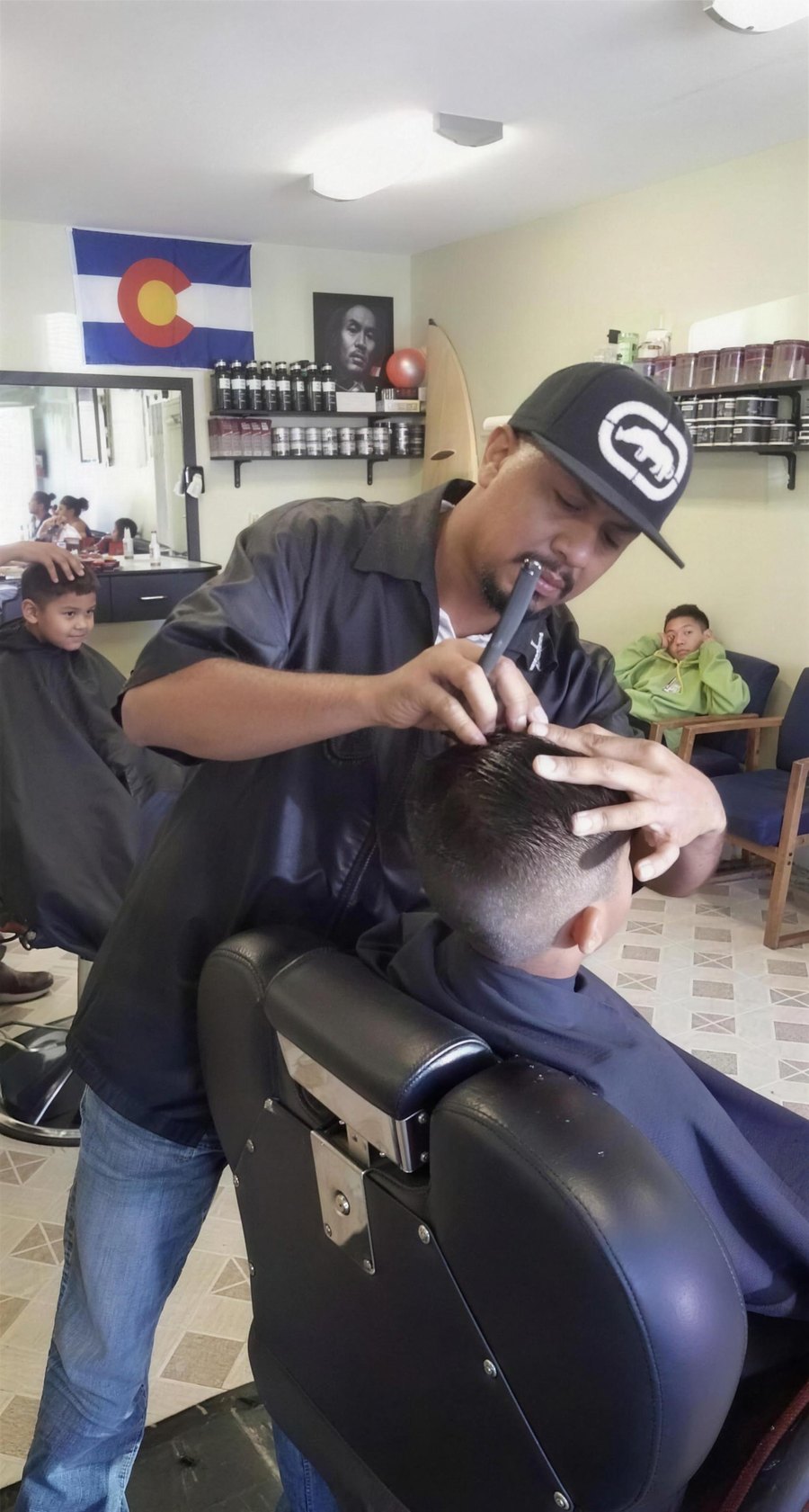 A young customer getting his hair cut at Champ's while others wait