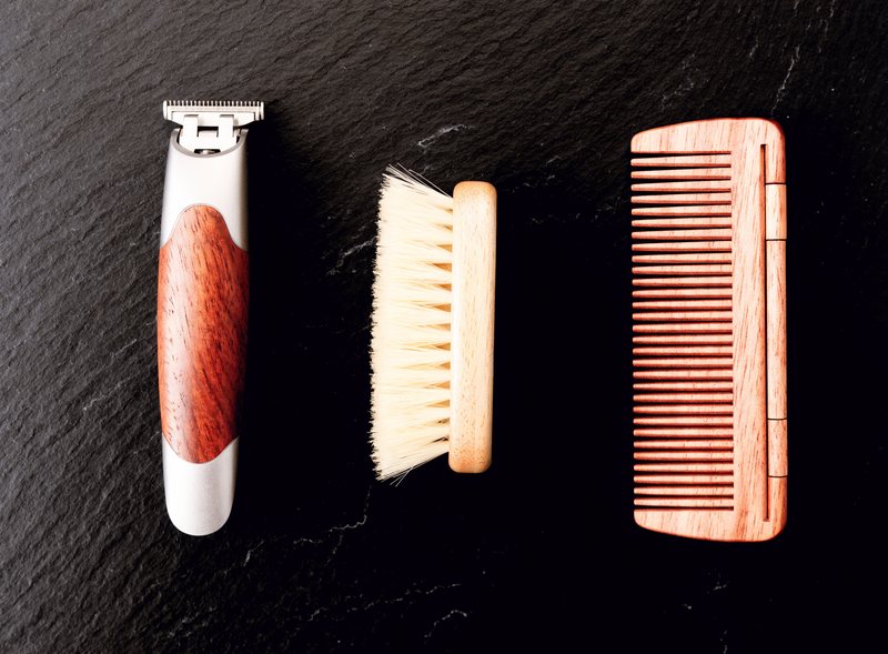Beard trimmer, brush and folding comb laid out on slate