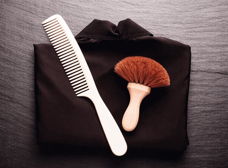 A folded barber cape with a comb and neck duster brush
